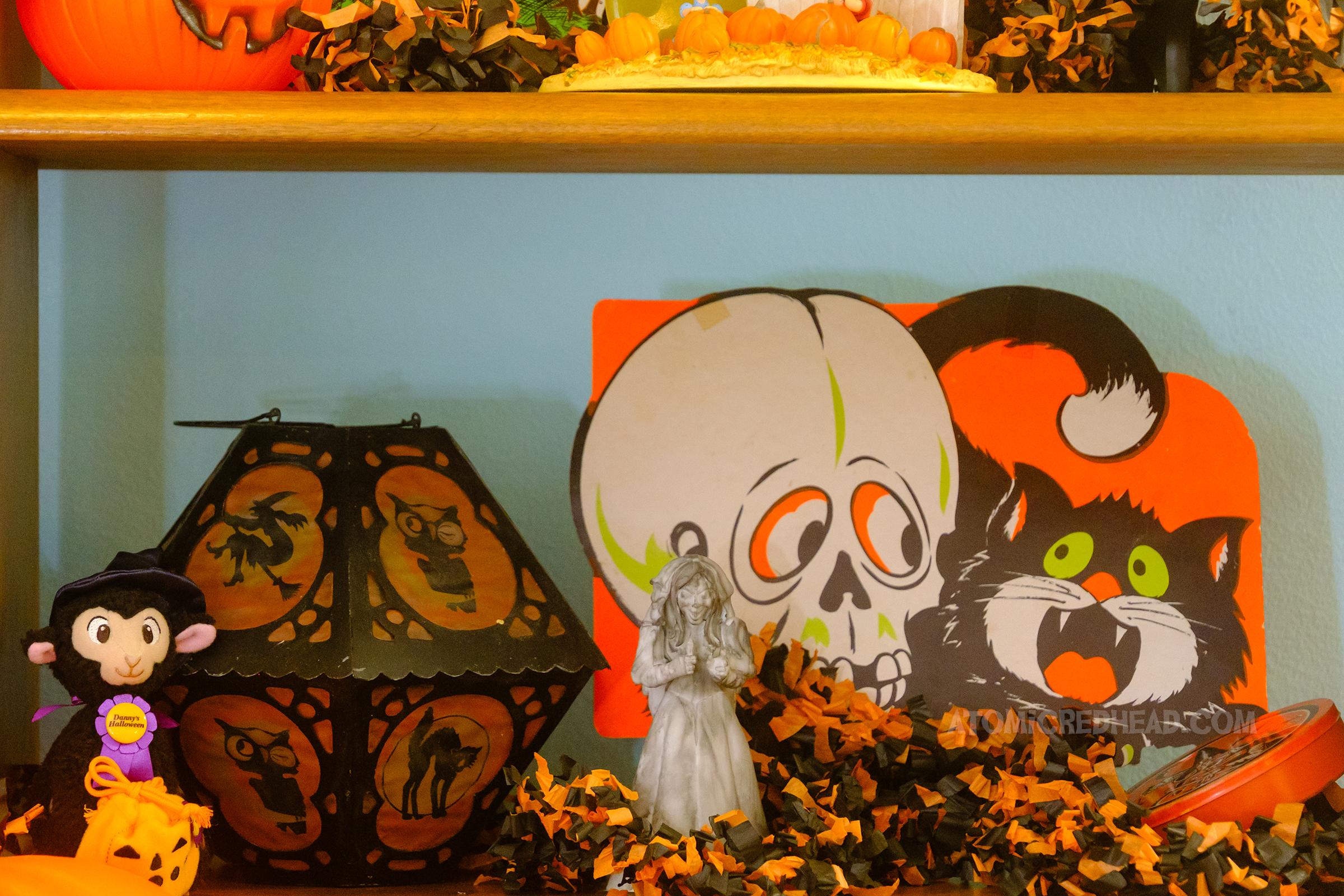 Close-up of a shelf with a retro lantern, a die cut of a black cat with a skull, a small figure of a ghostly bride.