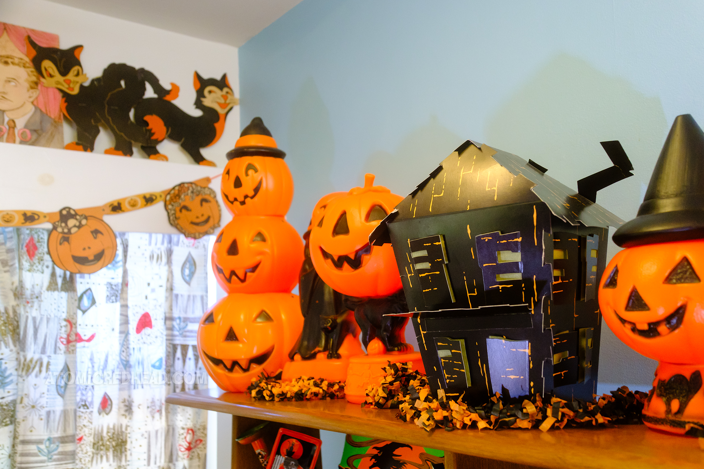 A paper haunted house rests among plastic jack o'lanterns.