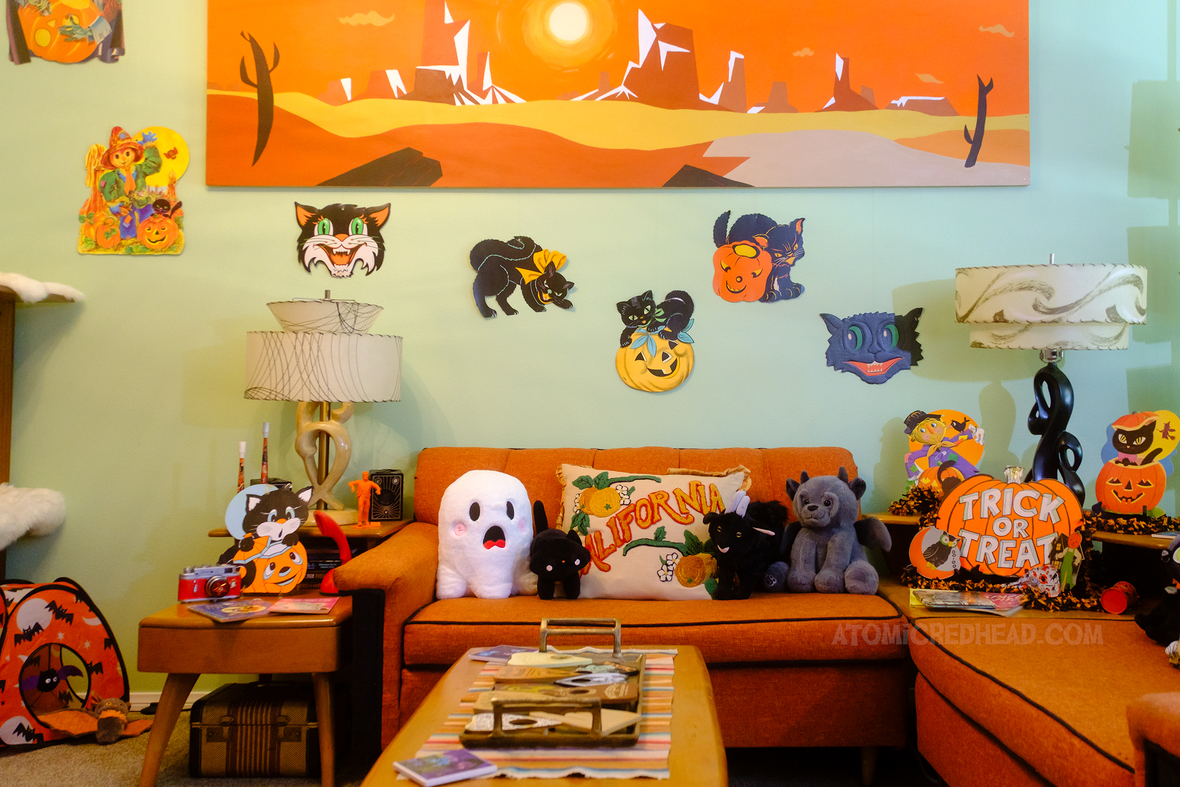 View over our couch, with has plushies of a ghost, black cat, goat, and gargoyle, above are die cuts of black cats.