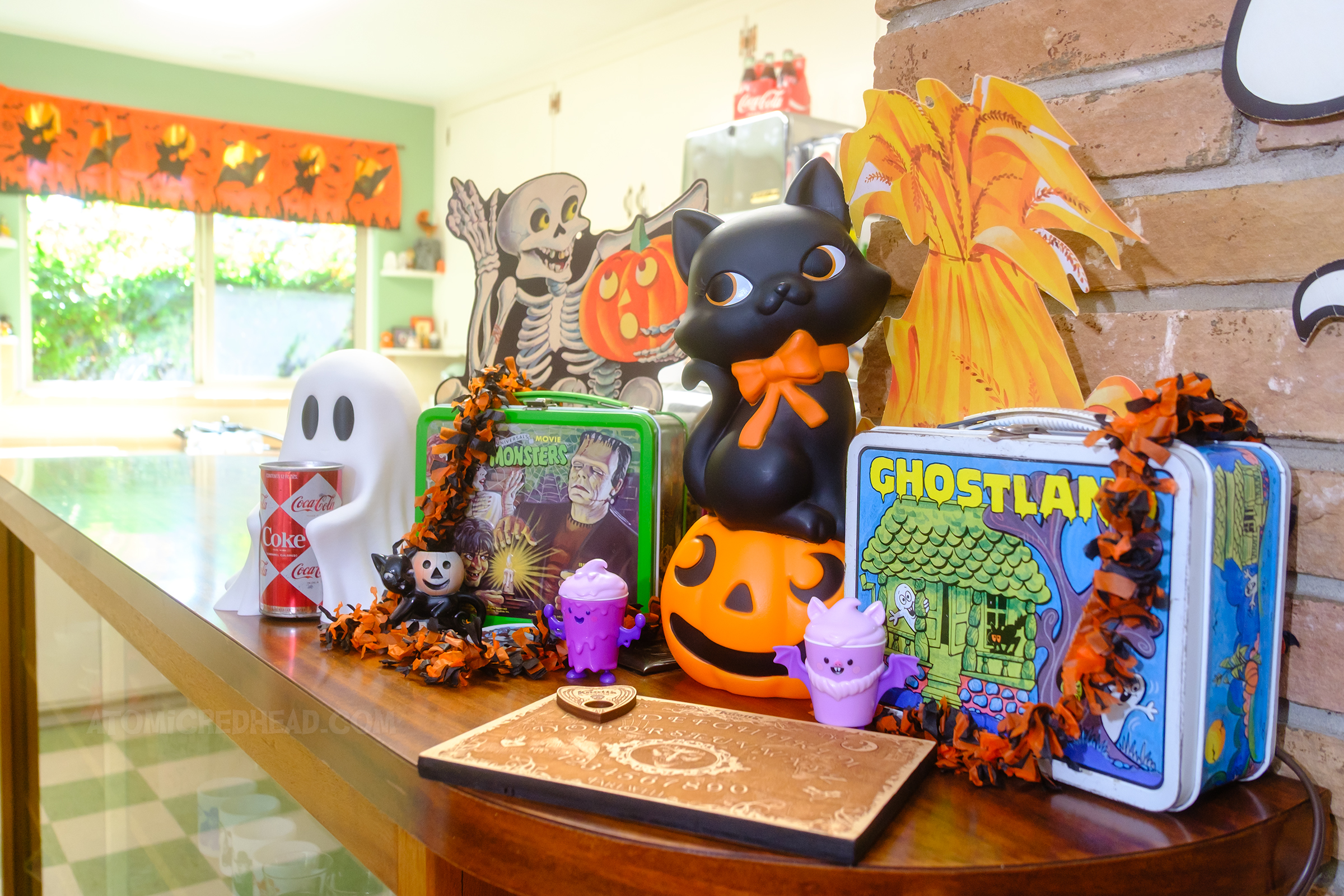 Vintage lunchboxes, one features movie monsters, another has ghosts in a haunted house, next to them is a small blow mold of a black cat on a jack o'lantern.
