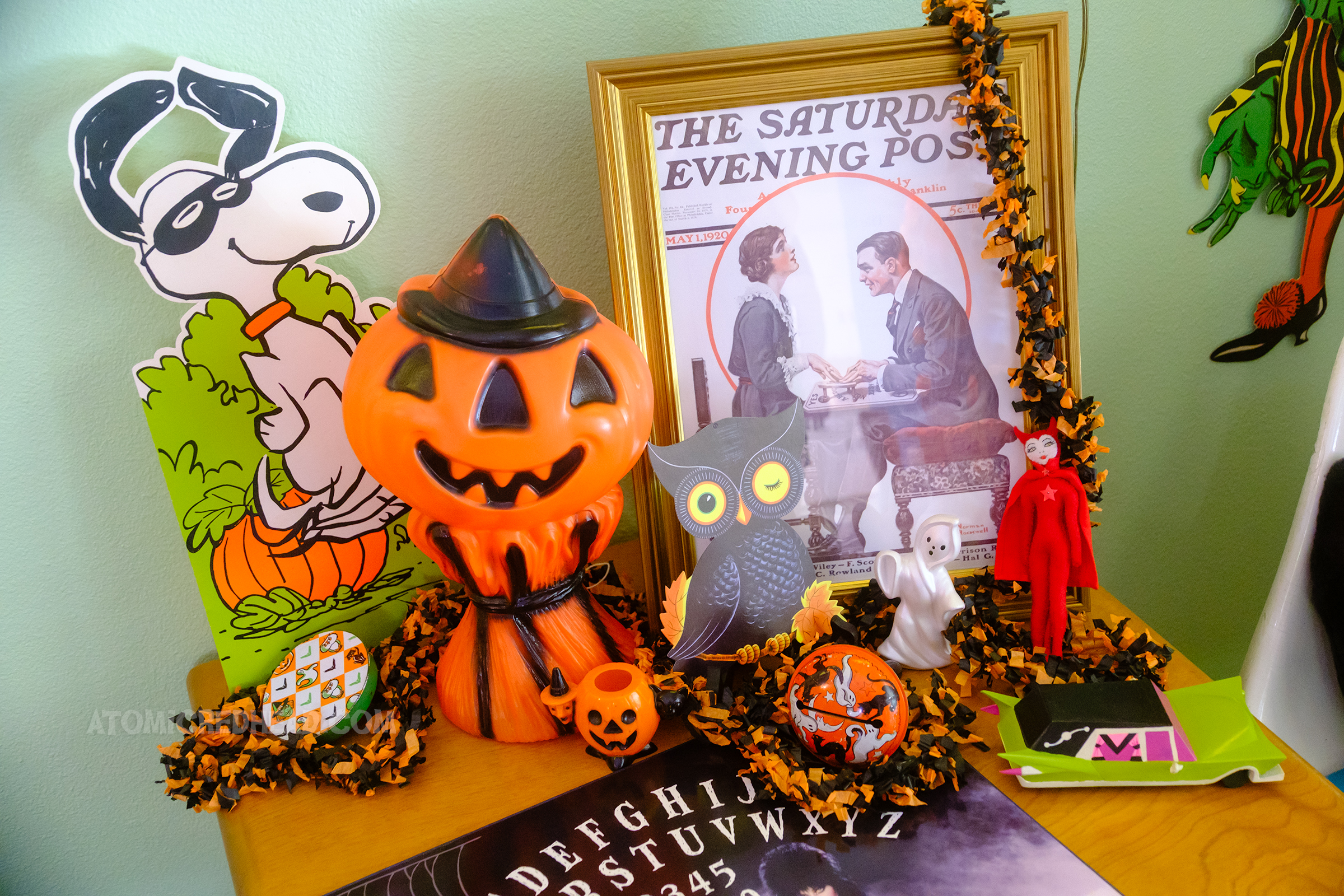Framed sits a cover of the Saturday Evening Post with a couple using a Ouija board. Next to it is a small blow mold of a jack o'lantern, and next to it is a standee of Snoopy dancing in a pumpkin patch.
