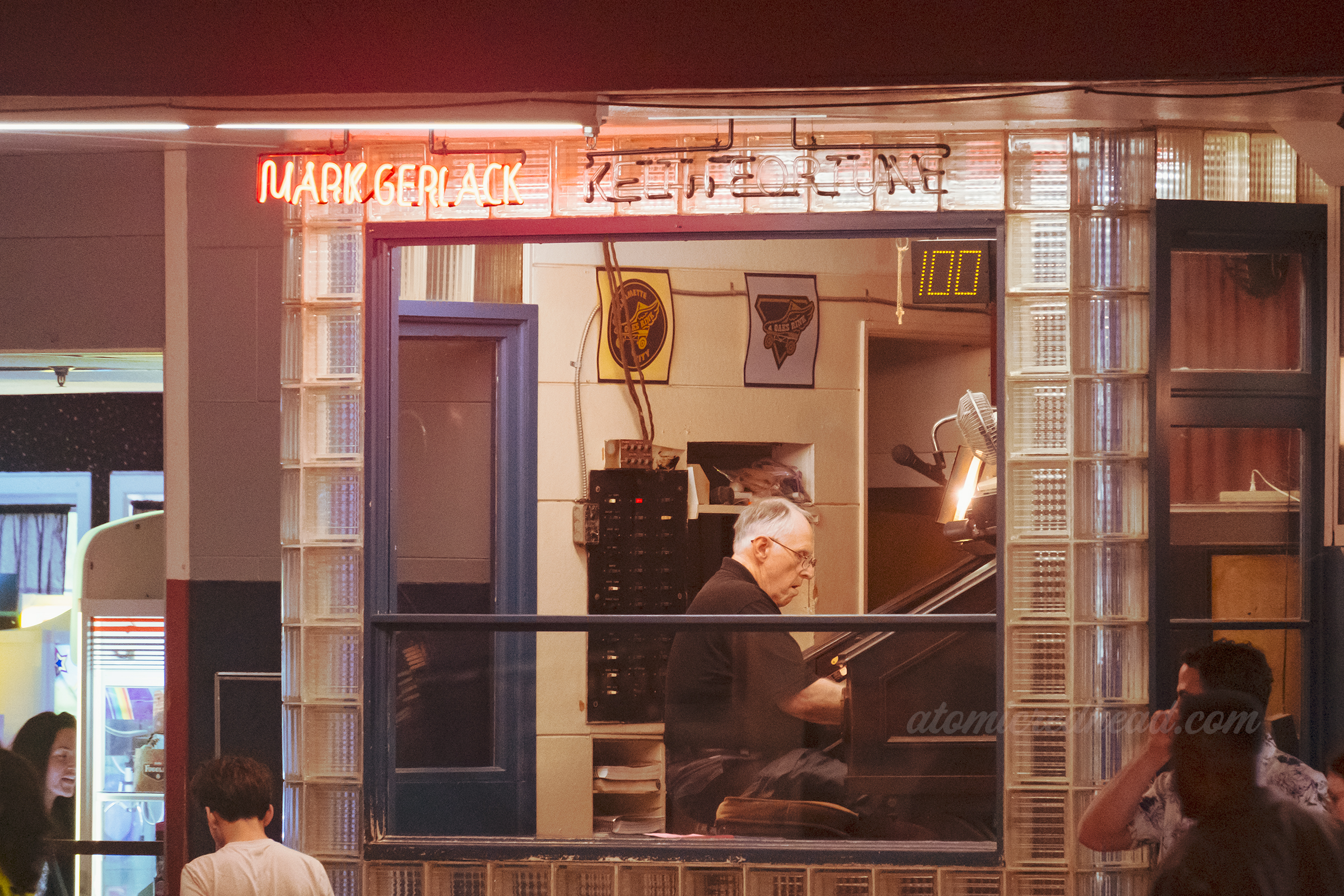 The roller rink organist behind a large pane of glass. Above is his name in red neon.