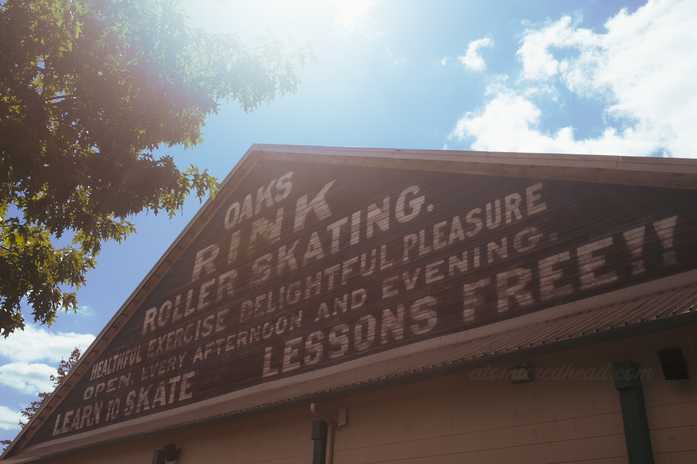 Exterior mural on the roller rink reading "Oaks Rink Roller Skating. Healthful exercise delightful pleasure open every afternoon and evening learn to skate lessions free!!"