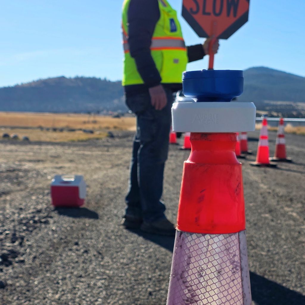An example of an Audible Cone sensor on a traffic cone with a safety worker working in the background.