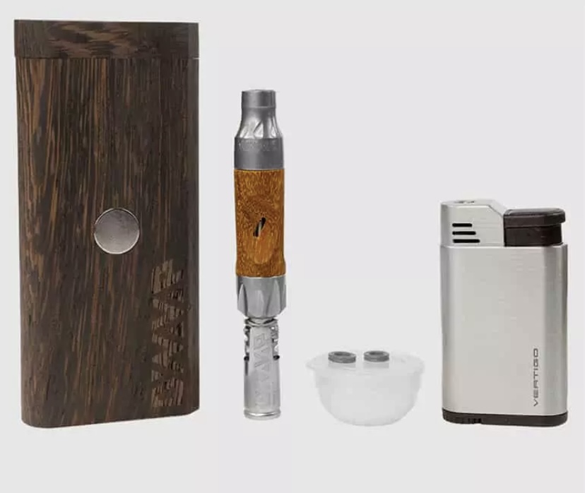 Wooden box beside a disassembled vape pen, and a small white container with two caps, plus a compact silver lighter on a light background.
