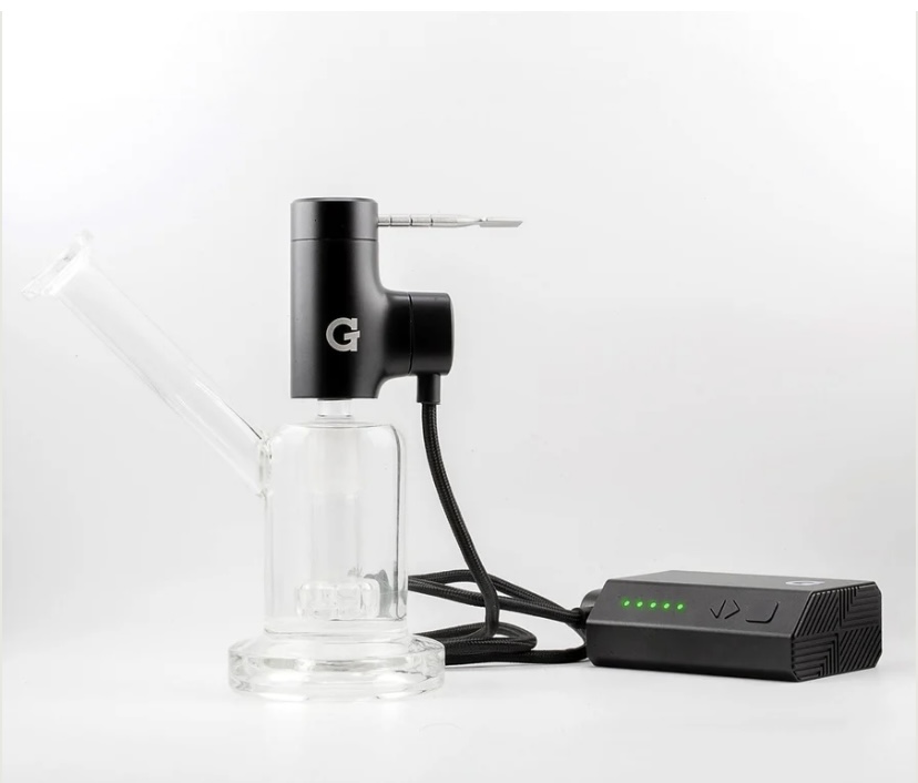 Electronic dab rig with a glass water chamber and a black heating unit connected to a battery pack with green LED indicators