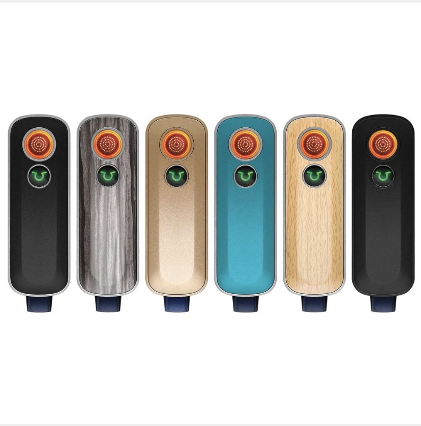 Six Juul-style Pod Vape Devices in a Row Each with a Circular Orange Mouthpiece and Green Indicator Light in Black Gray Wood Bronze Teal Light Wood and Black Finishes - Australia E-cigarette Store
