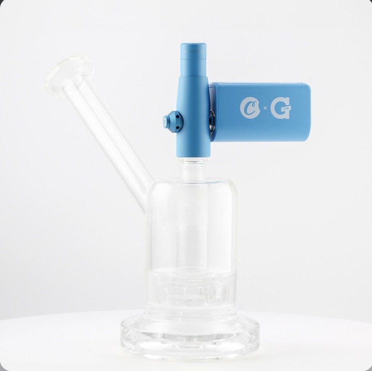 Clear glass bong with a blue modular attachment mounted on the neck, placed on a white surface.