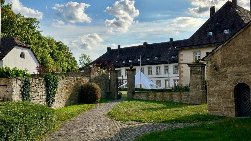 Einfahrt zum Schlosshotel Gehrden mit historischem Gemäuer, Kopfsteinpflasterweg und Blick auf das Hauptgebäude