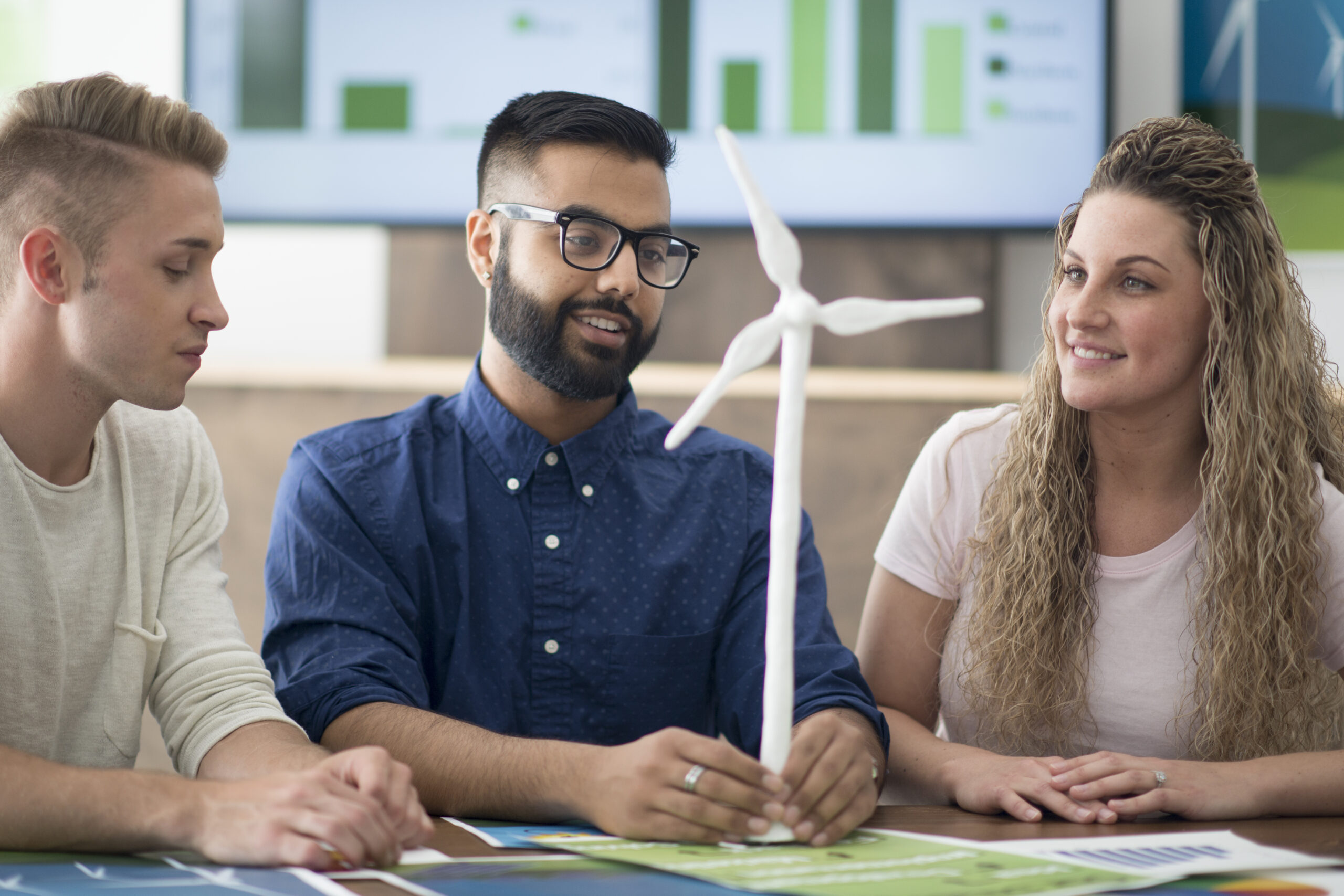 A multi-ethnic group of young adult entrepreneurs are working on a project with wind turbines for alternative energy sources. They are holding a model of a wind turbine.