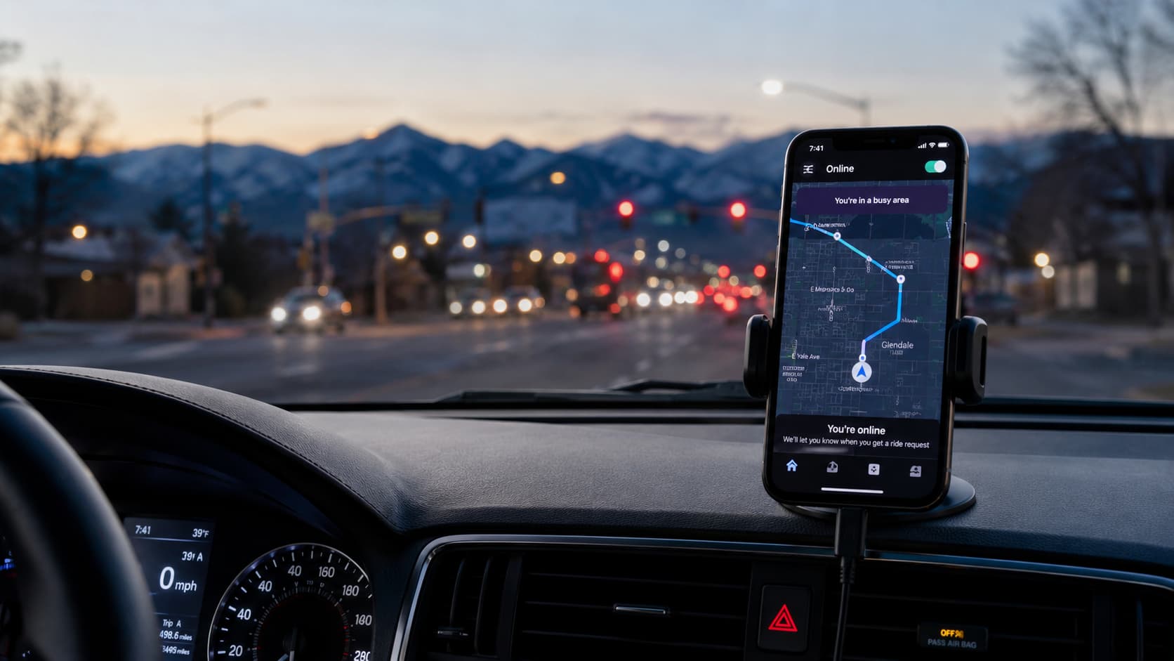 Smartphone mounted on a car dashboard displaying a rideshare driver GPS route while driving through a Colorado suburban road at dusk with mountain silhouettes in the background.