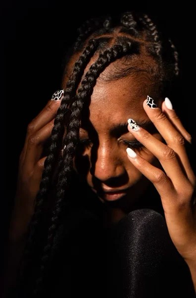 Black woman with braided hair holding her head in distress, symbolizing anxiety and emotional overwhelm