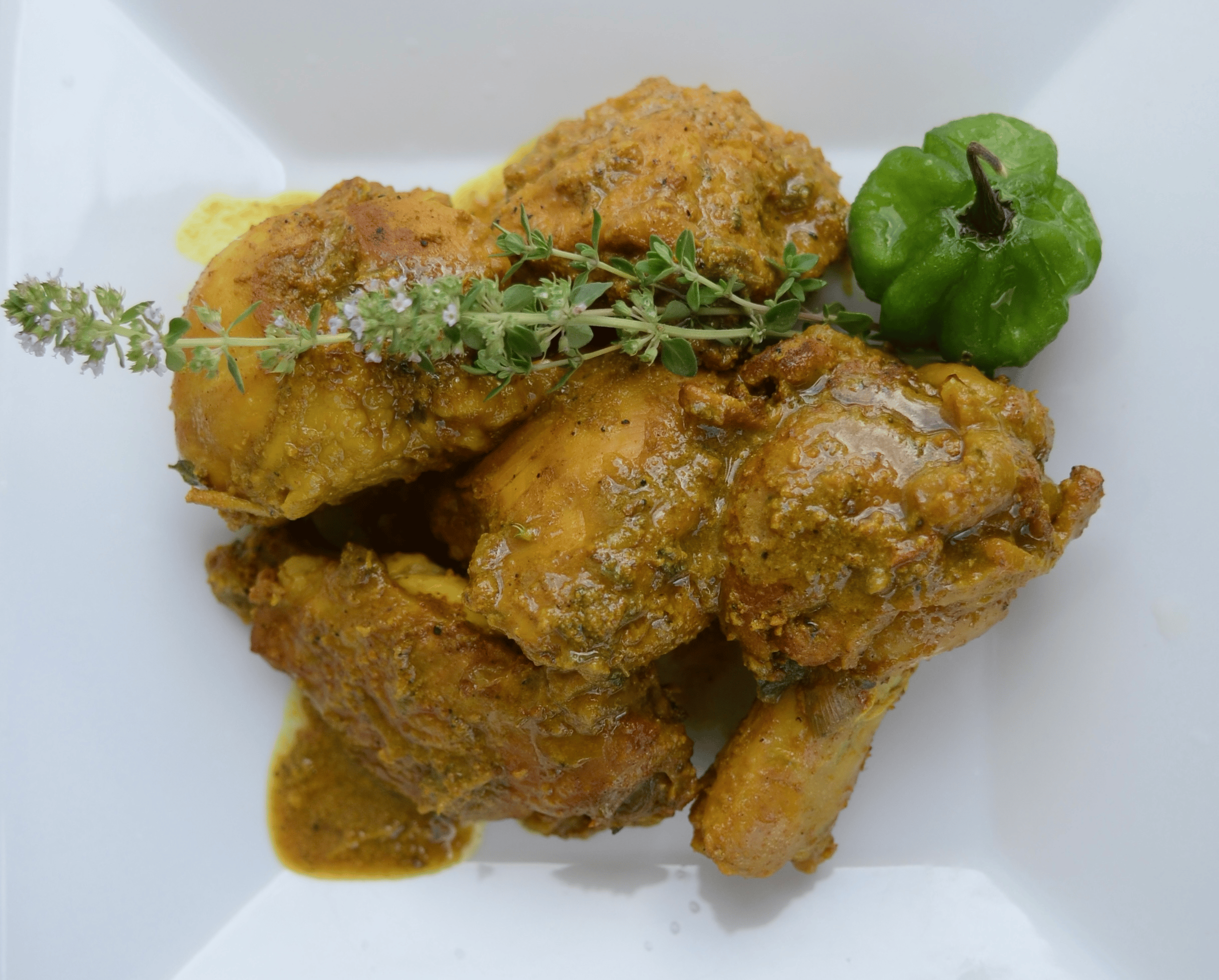 Jamaican curry chicken garnished with herbs and a Scotch bonnet pepper, prepared by Chef Nadine.