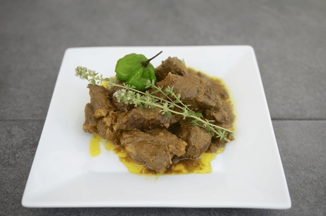 Jamaican curry goat garnished with herbs and a Scotch bonnet pepper, prepared by Chef Nadine.