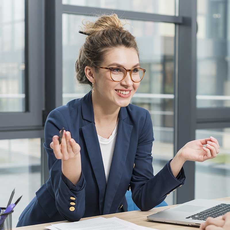Professional woman in a blue blazer and glasses engaging in a lively discussion at the office.