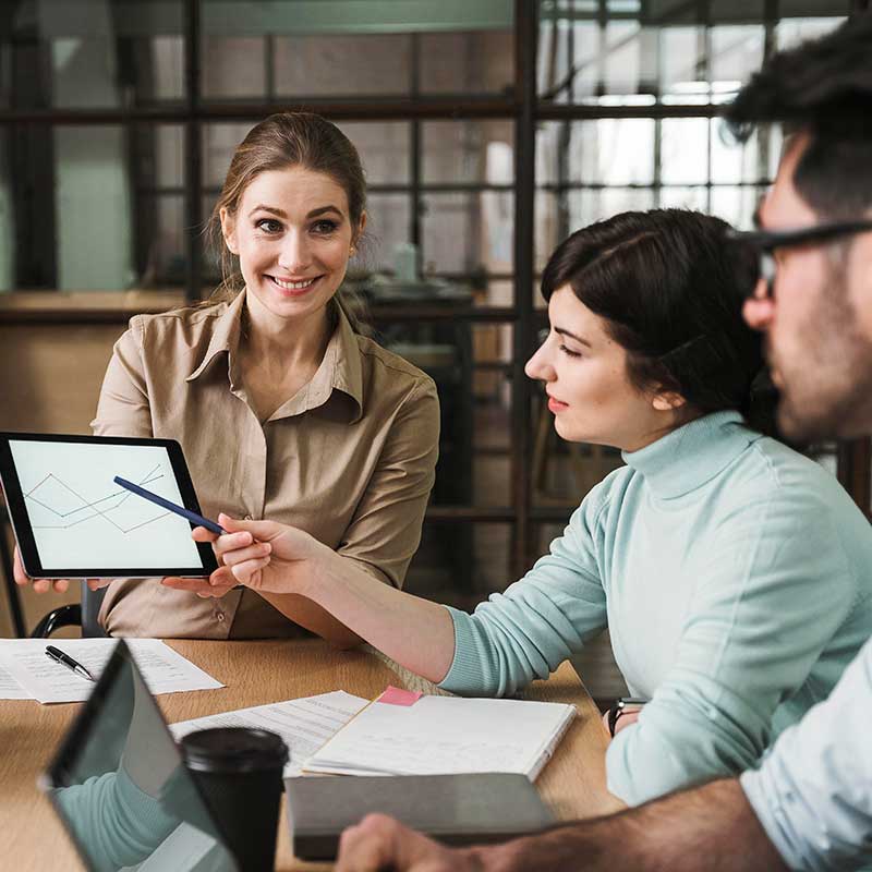 A confident businesswoman presents a graph on a tablet to her colleagues during a team meeting.