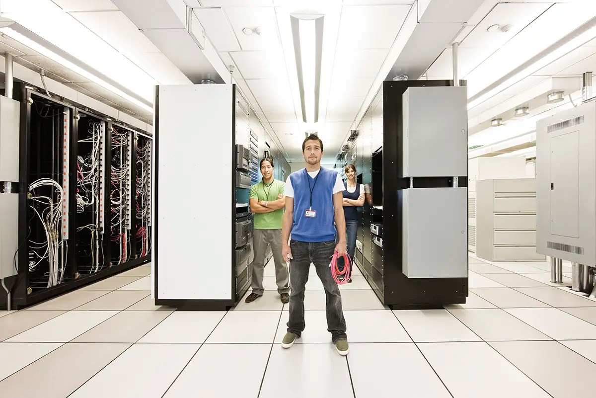 Web hosting support team standing in a data center between server racks