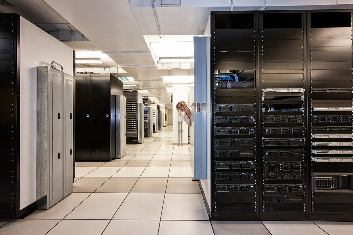 Data center with server racks and a woman peeking from behind a cabinet.