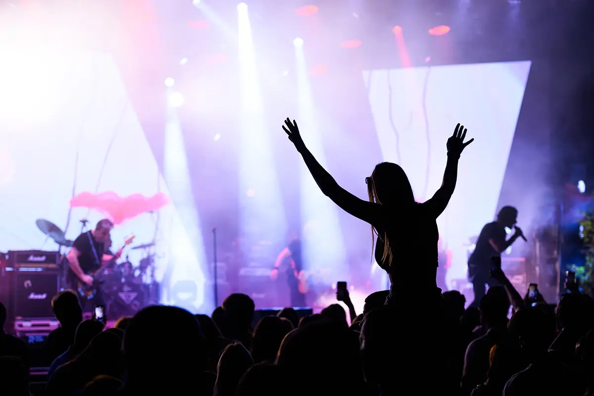 Excited crowd at a live event with colorful stage lights and musicians performing