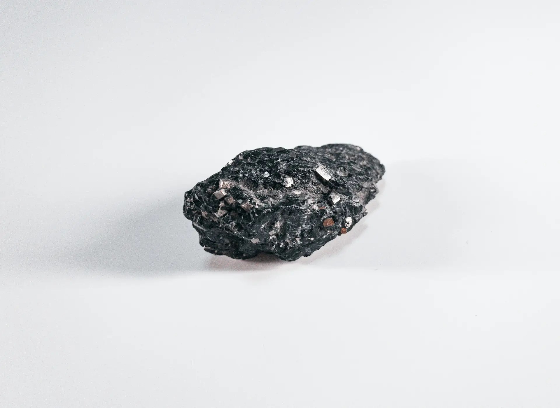 A small, dark chunk of biotite mineral, showing shiny, flaky, black-to-dark-brown crystals embedded in a rough matrix, against a white background.