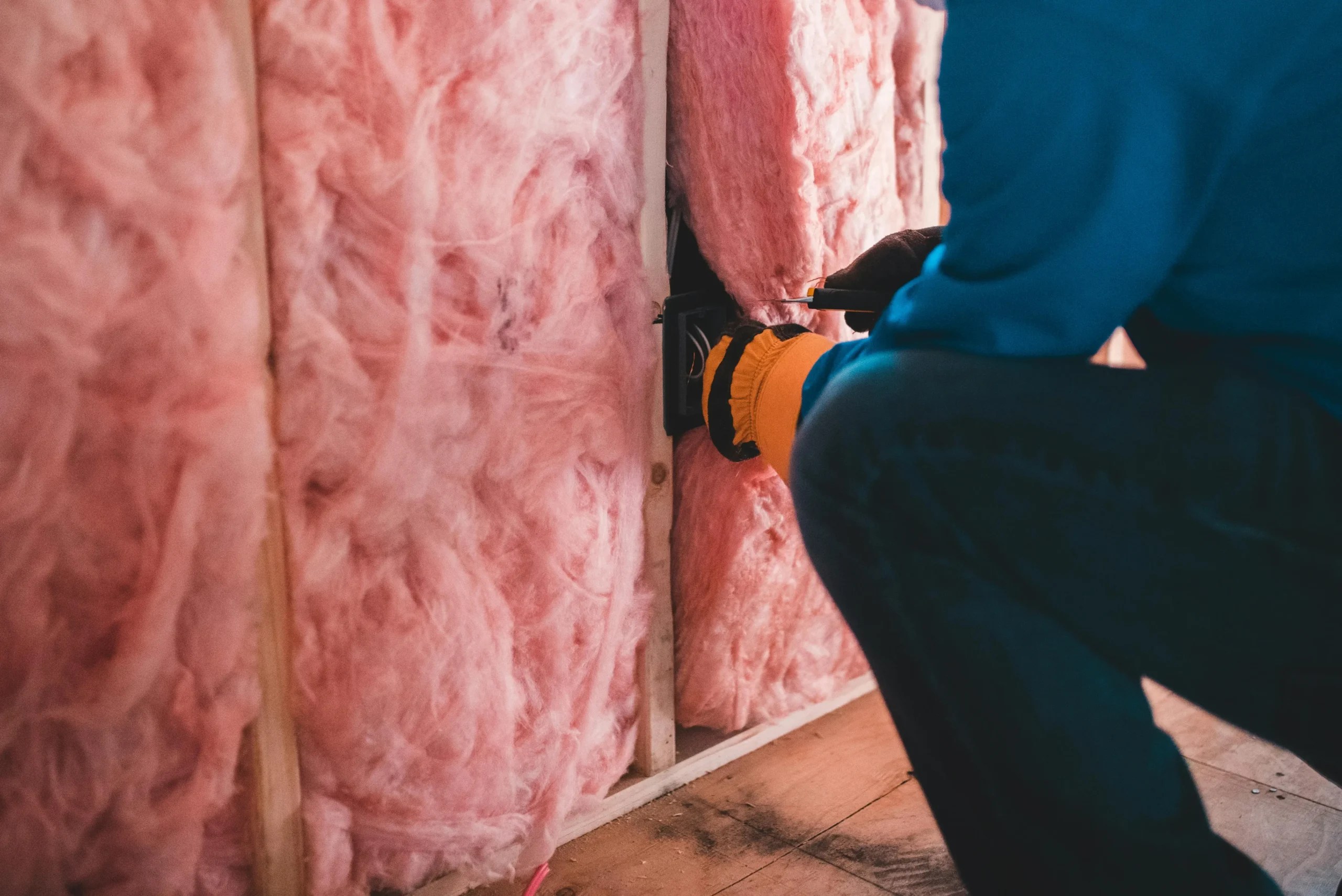 A man installs pink thermal insulation on a wall, focusing on proper placement and securing the material.