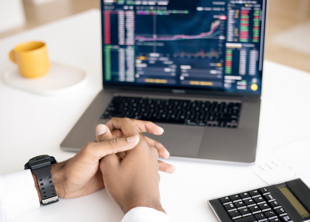 An investor's hands on a laptop keyboard with stock charts displayed on the screen.