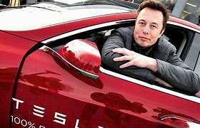 Elon Musk smiling in the driver’s seat of a Tesla Model 3.