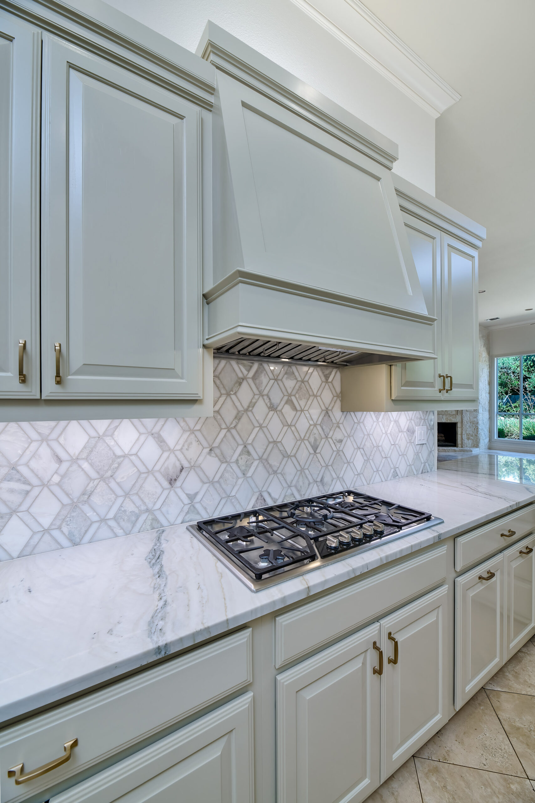 Sage green kitchen cabinets with custom range hood, gas cooktop and marble backsplash in San Antonio