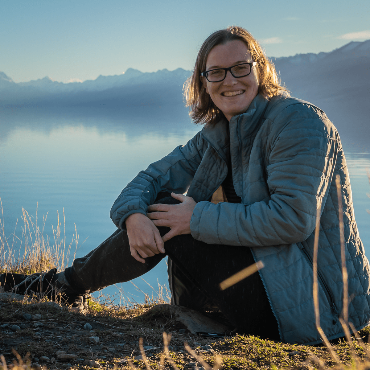 Xandra zit glimlachend bij een bergmeer in Nieuw-Zeeland