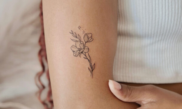 Small fine line wildflower tattoo with delicate leaves and blossoms placed on the inner arm