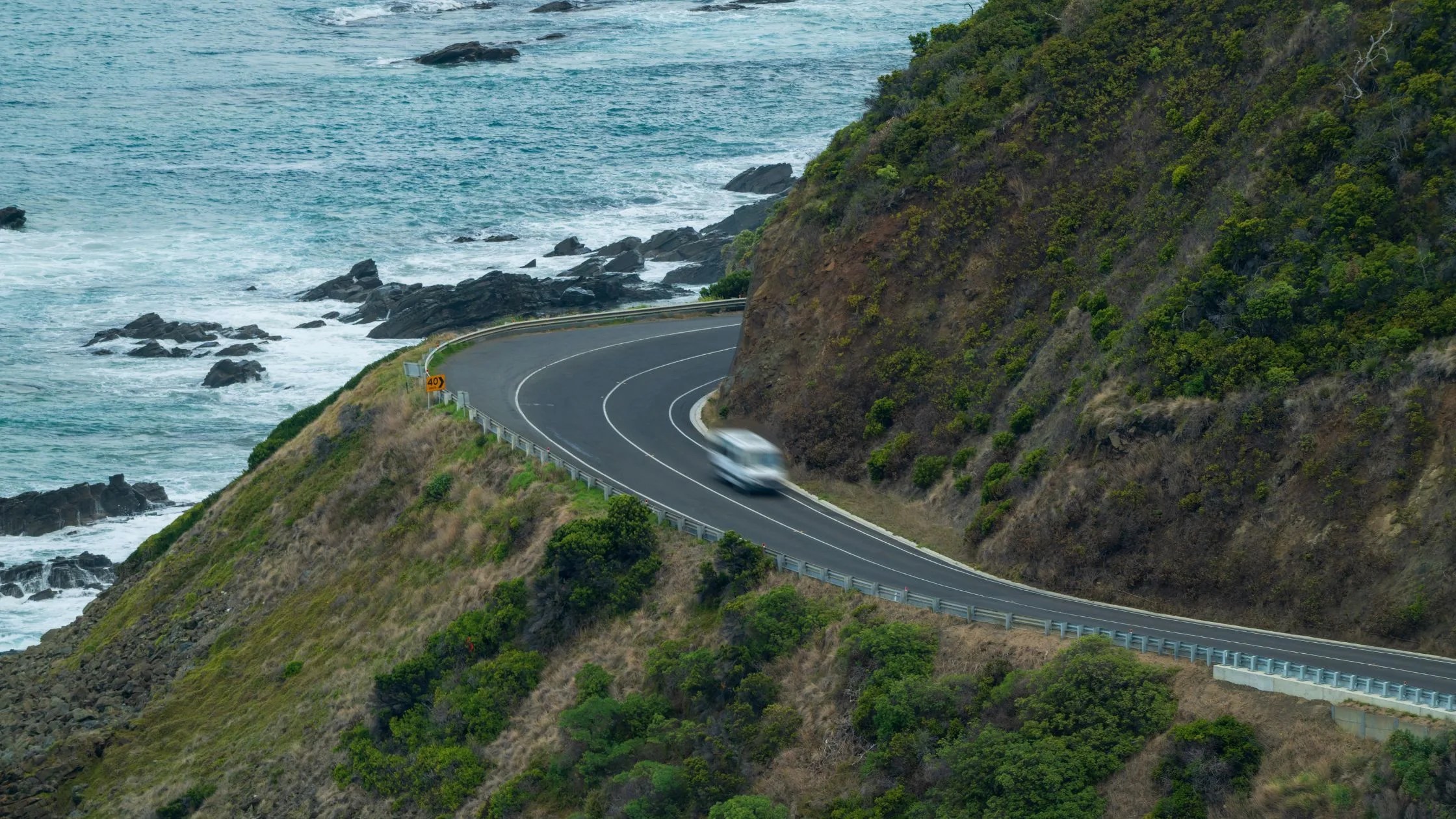 a vehicle going very fast around a sharp turn on a mountain cliff with guardrail
