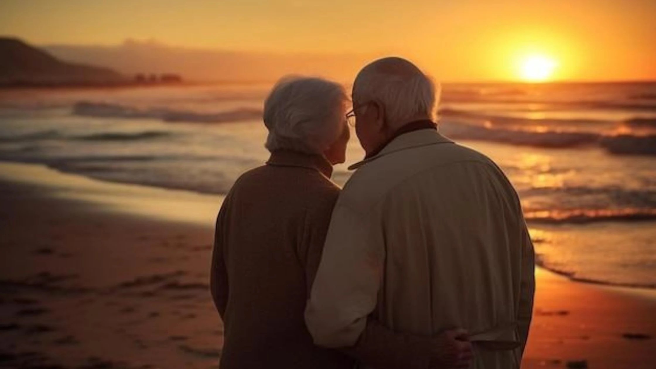 older married couple embracing on beach at sunset
