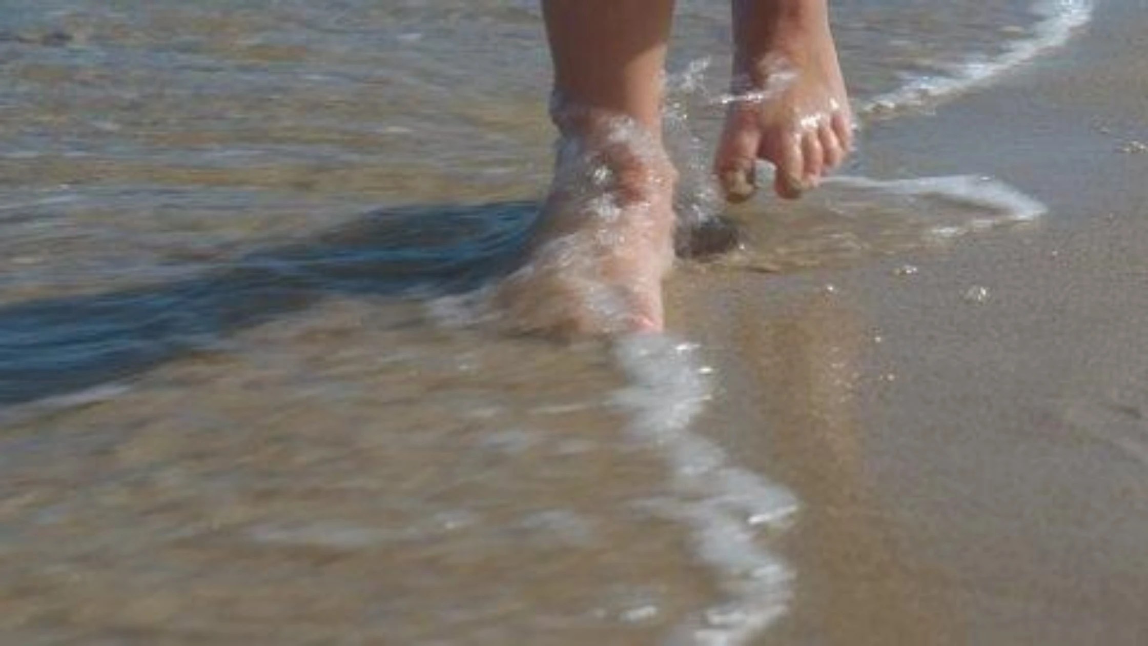 child's feet walking on beach with water washing over them