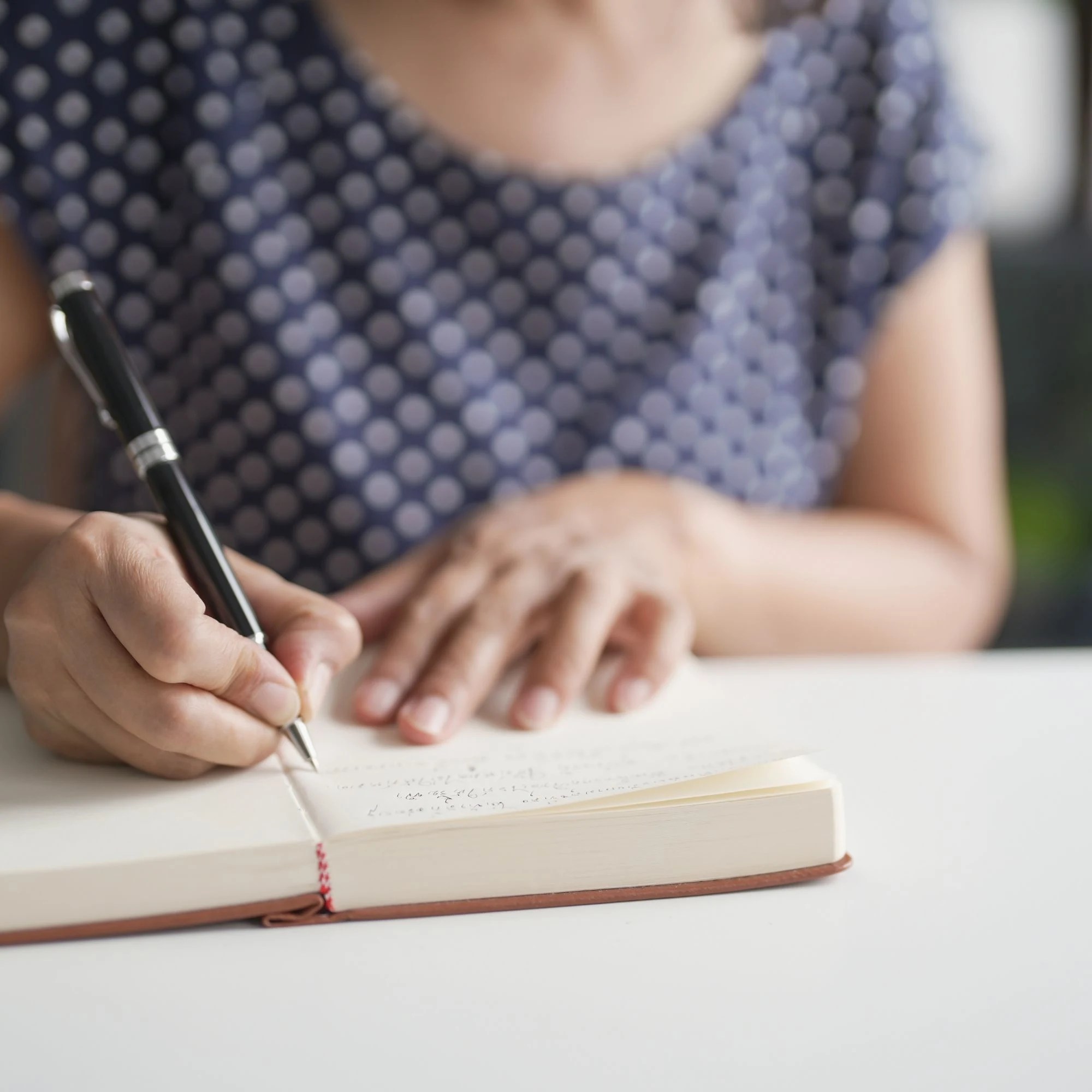 woman sitting at table writing in an open journal