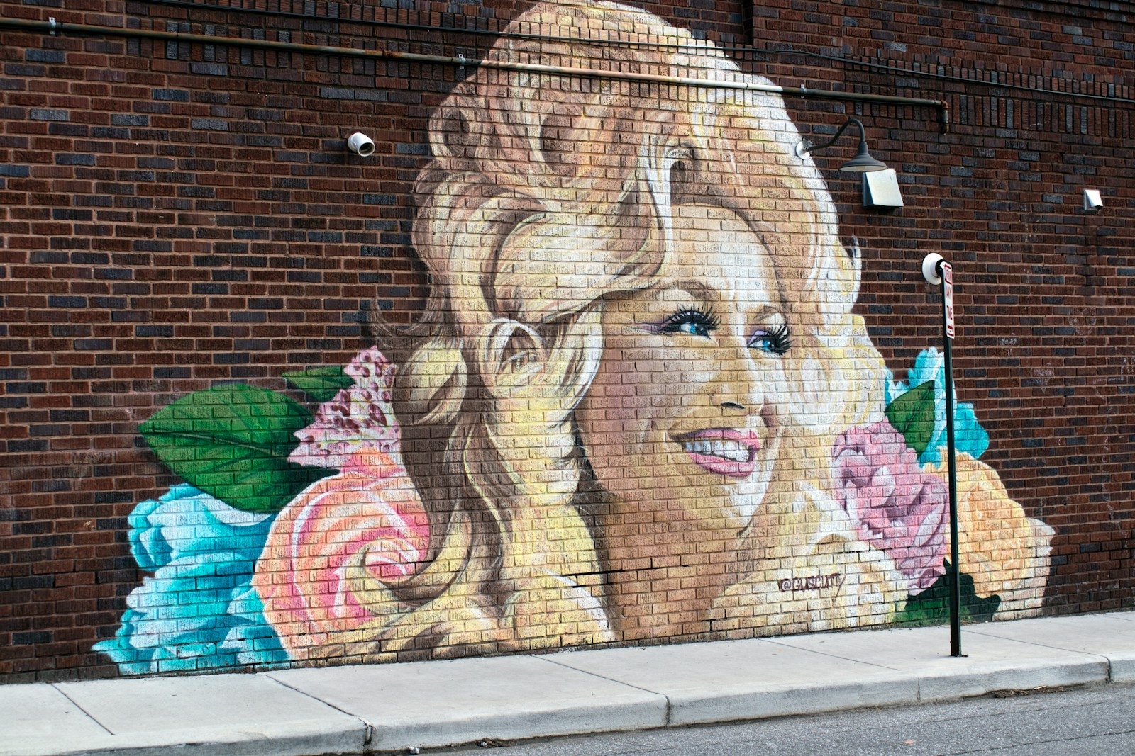 Mural of Dolly Parton painted on a brick wall surrounded by flowers