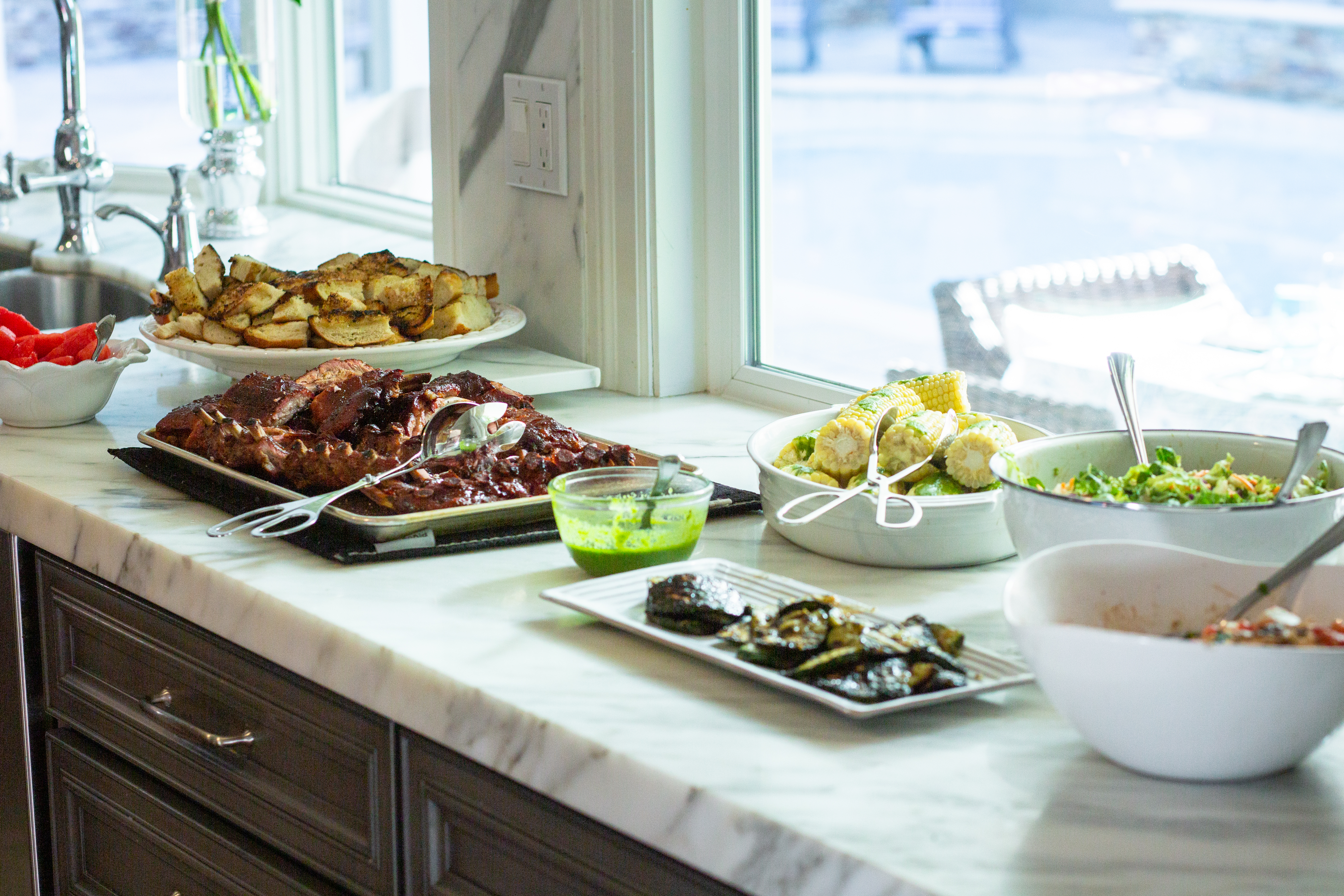 Table at bbq potluck with ribs, corn, veggies and more.