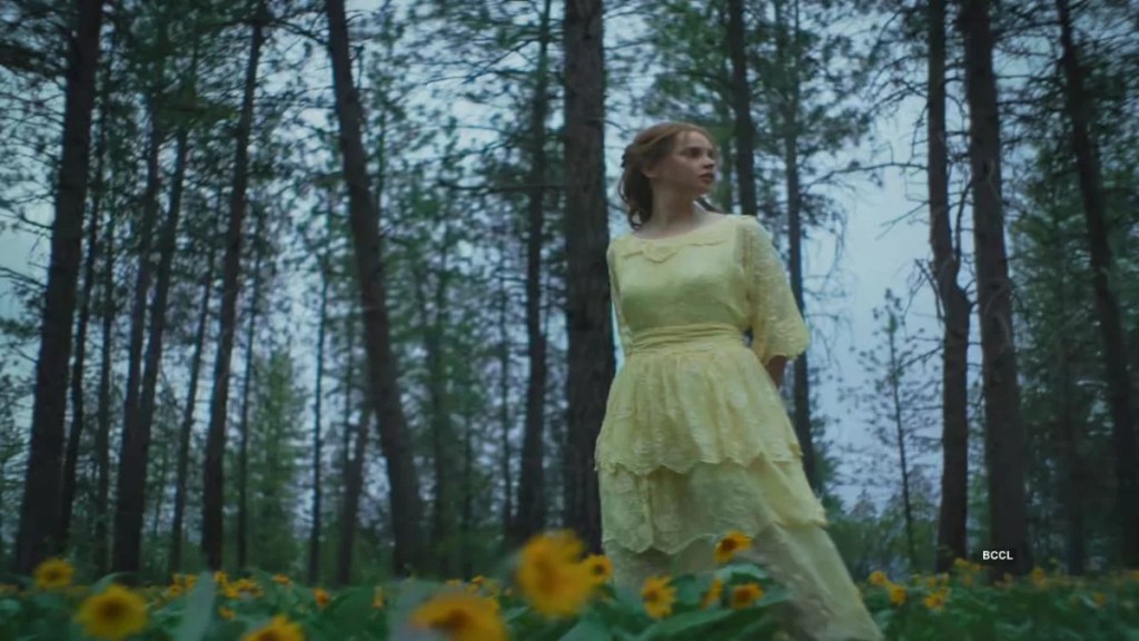 Felicity Jones as Gladys Olding standing in a field of yellow wildflowers in a forest.