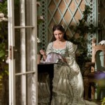 Actress Connie Jenkins-Greig as young Violet Bridgerton seated near a garden trellis while working on embroidery.