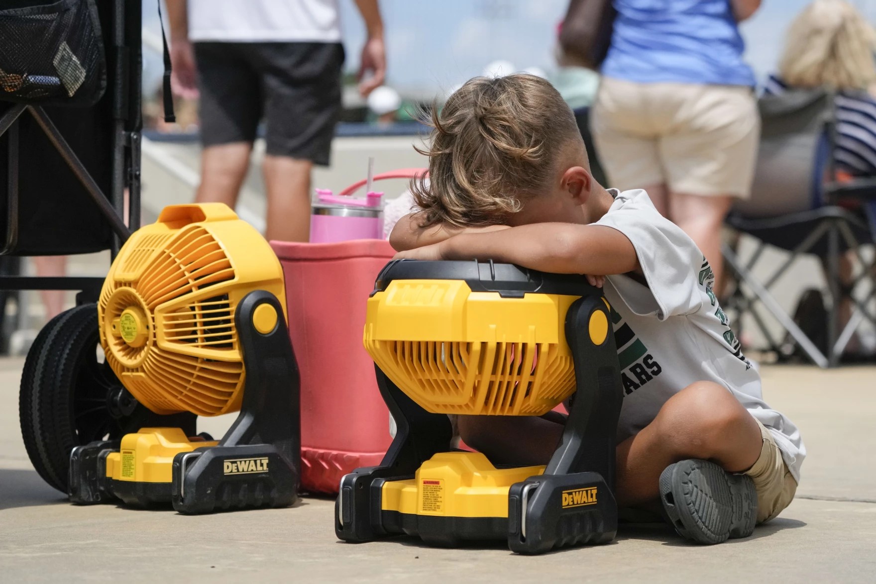 A child leans against a fan for relief from the heat.