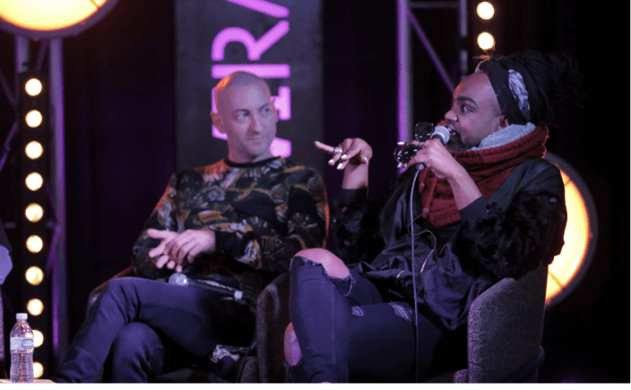 Two artist on stage talking on a panel