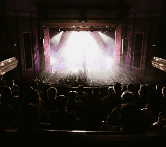 the view from behind the audience looking at a stage, the stage is filled with light