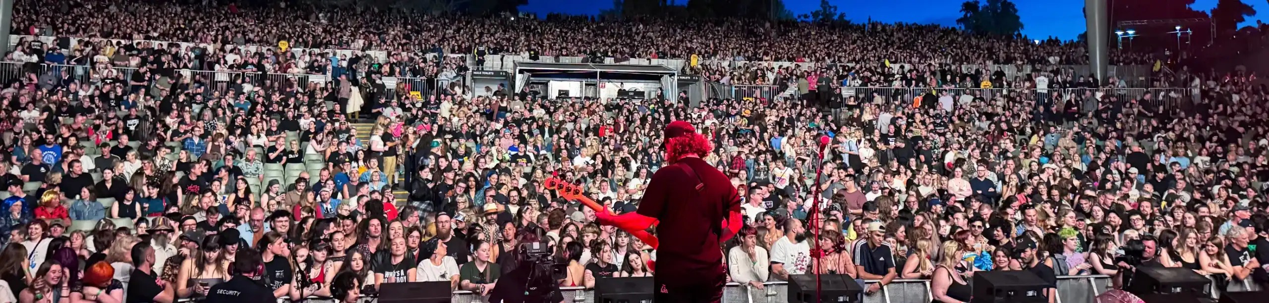 A person with a guitar on stage, you can see the crowd in front of them