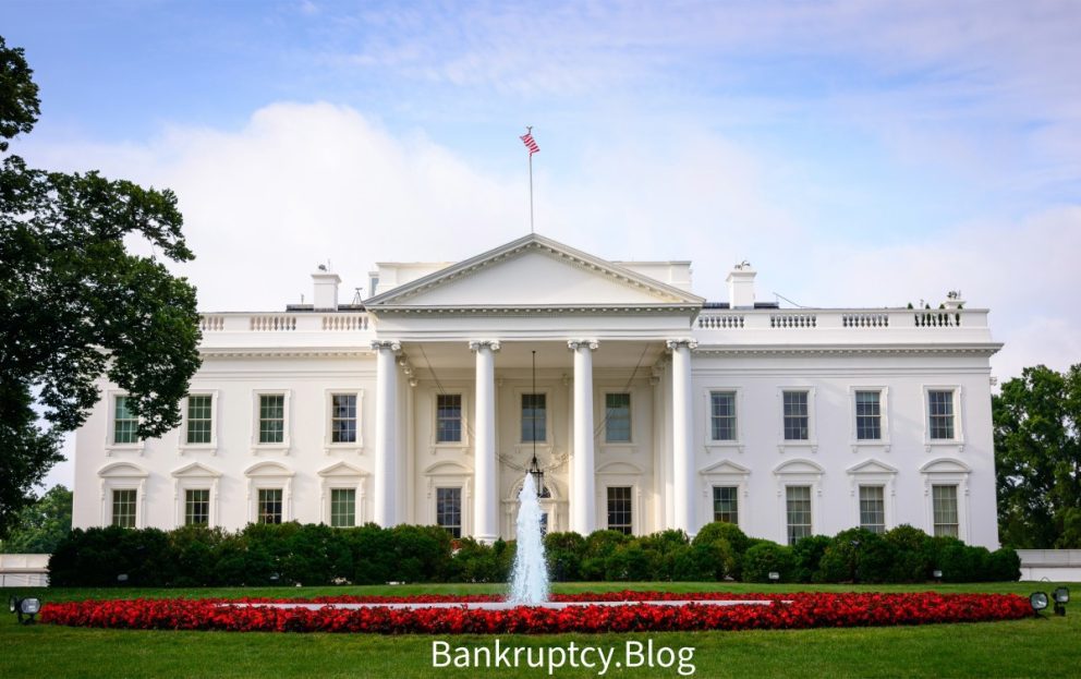 The White House with a fountain in front and a flowerbed of red flowers, under a clear sky, with the text ‘Bankruptcy.Blog’ overlaying at the bottom as the Biden Administration provides student loan forgiveness for borrowers under the PSLF.