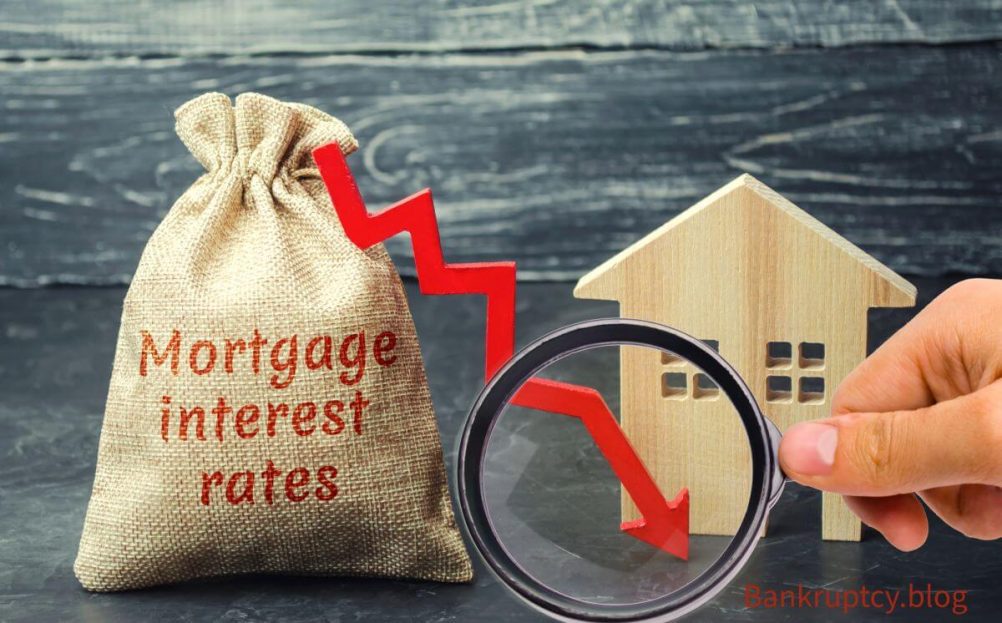 A burlap sack with the words ‘Mortgage interest rates’ printed in red, a downward-pointing red arrow signifying a decrease, and a magnifying glass focused on a small wooden house model against a dark wooden background. The image suggests an analysis or scrutiny of falling mortgage interest rates, relevant to financial topics discussed on bankruptcy.blog such as paying off credit card debt.