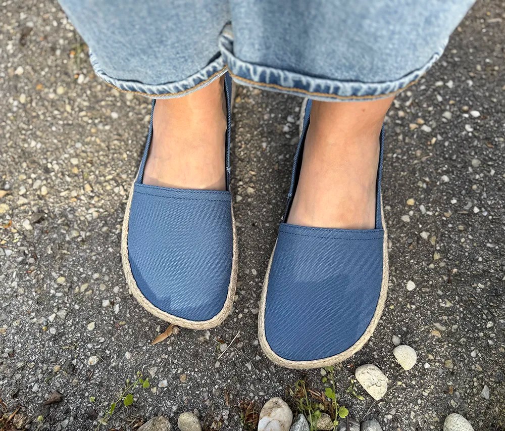 Top view of Shapen Playa blue barefoot espadrilles worn on feet with rolled-up jeans, standing on textured pavement