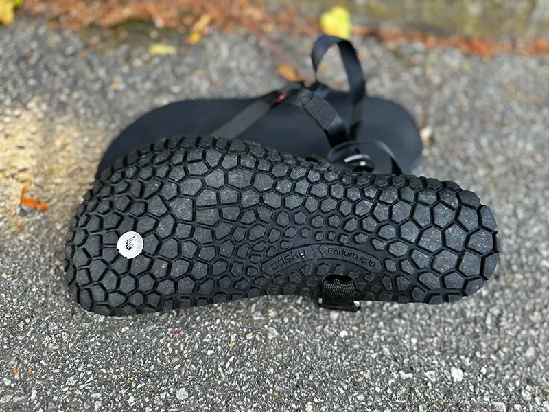 Close-up of Bosky barefoot sandal showing hexagonal Enduro Grip outsole tread, placed on textured asphalt