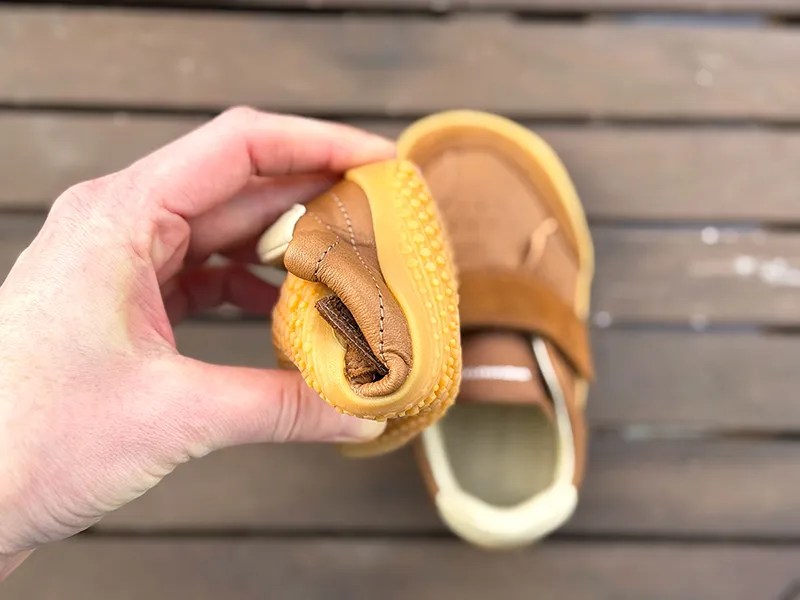 Hand bending a flexible brown kids barefoot shoe with yellow sole