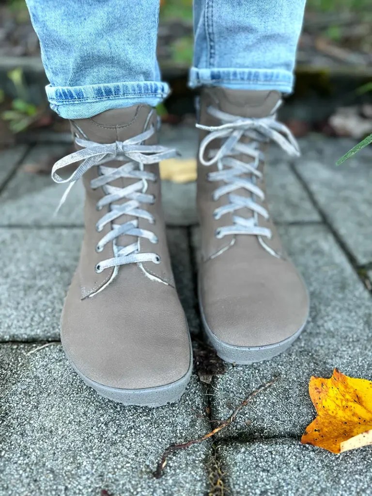 Taupe suede barefoot boots shown with jeans on gray pavement.