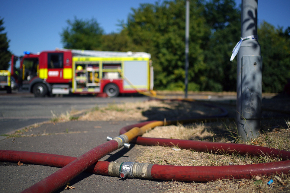 A fire engine at the rear of the image with a hose on the ground at the front