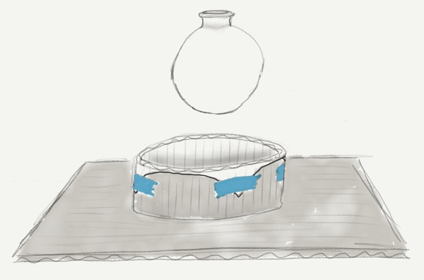 A depiction of a cardboard surface, out of which rises a cardboard cylinder, on top of which is taped down a sheet of Worbla, into which a glass globe will be lowered